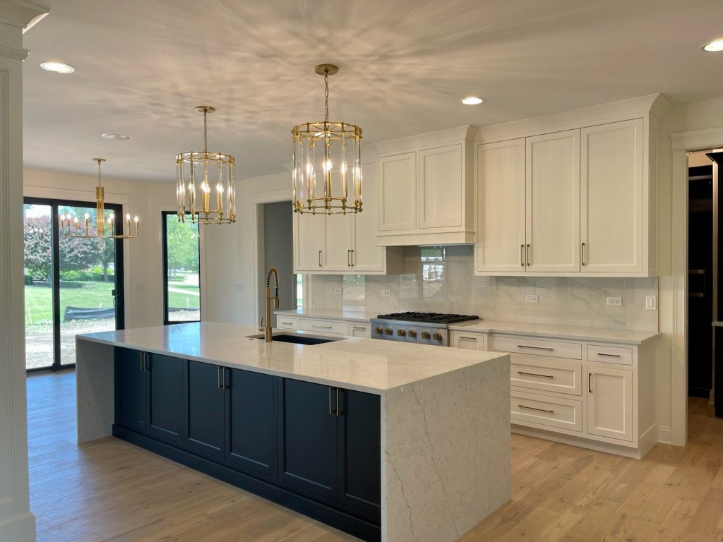Remodeled kitchen with navy island, quartz waterfall counter and brass pendants